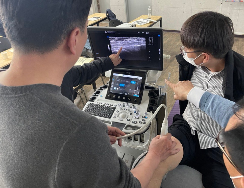 여러 명이 초음파 기기로 팔에 초음파 검사를 하고 초음파 화면을 보고 있다 — 대한한의영상학회 초음파 약침·도침 강의 | 서울 바로한의원