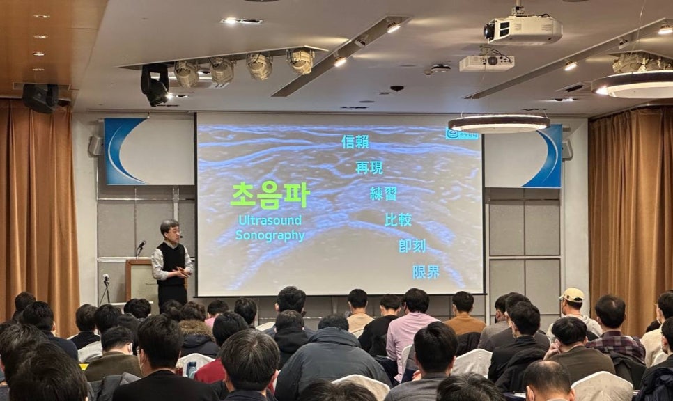 강사가 강단에서 초음파 관련 내용을 대형 스크린에 띄워놓고 청중에게 설명하고 있는 모습 — 대한한의영상학회 초음파 약침·도침 강의 | 서울 바로한의원