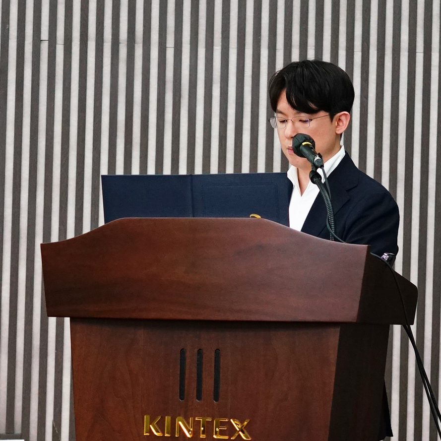 안경을 쓴 남성이 마이크가 있는 나무 연단에서 강연하고 있다 — 대한한의영상학회 초음파 약침·도침 강의 | 서울 바로한의원 안태석 원장