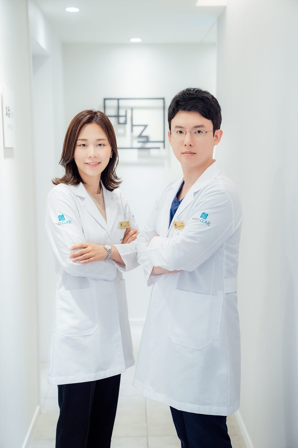 밝은 복도에서 흰색 가운을 입은 남녀 의사 두 명이 팔짱을 끼고 서 있다 — 서울 바로한의원 초음파 약침·도침