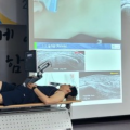 한 사람이 테이블에 누워 있고, 뒤쪽 스크린에 초음파 영상과 시술 장면이 보인다 — 초음파 유도하 약침 시술 | 서울 바로한의원