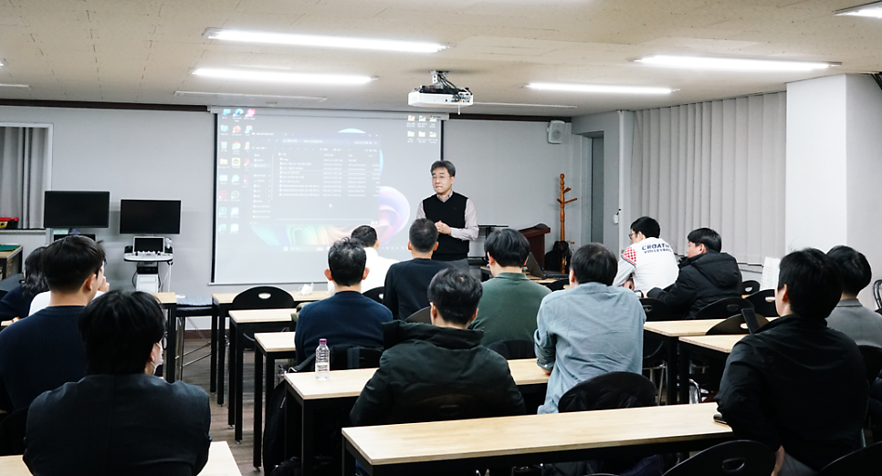 강사가 스크린 앞에서 수강생들에게 강의하고 있으며, 왼쪽에 초음파 기기가 보인다 — 대한한의영상학회 초음파 약침·도침 강의 | 서울 바로한의원