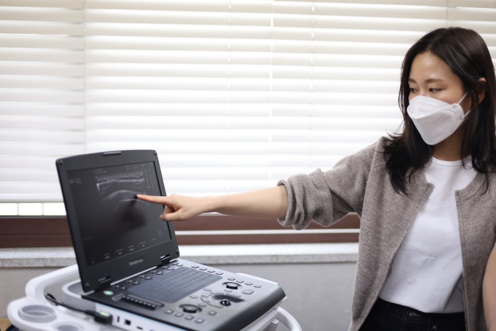 마스크를 쓴 여성이 초음파 기기 화면을 손가락으로 가리키고 있다 — 초음파 정밀 진단 | 서울 바로한의원 초음파 약침·도침·침도