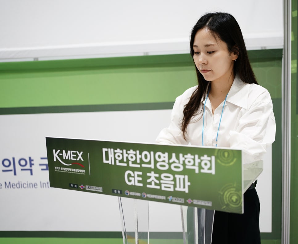 흰 셔츠를 입은 여성이 '대한한의영상의학회 GE 초음파'라고 적힌 연단 뒤에 서 있다 — 대한한의영상학회 초음파 약침·도침 강의 | 서울 바로한의원 문지현 원장