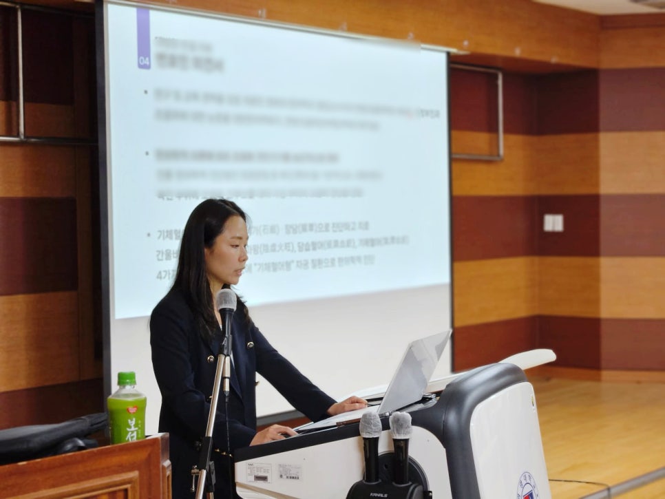 한의과대학 초청 강연에서 강사가 마이크 앞에서 노트북을 보며 발표하는 모습 — 대한한의영상학회 초음파 약침·도침 강의 | 서울 바로한의원
